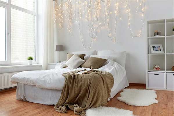 Bedroom painted in while with string lights and khaki cover and pillows showing how bedroom pain in neutral shades makes room more relaxing